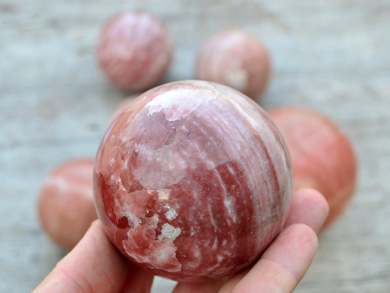One rose calcite ball crystal 65mm on hand with background with some balls on wood table
