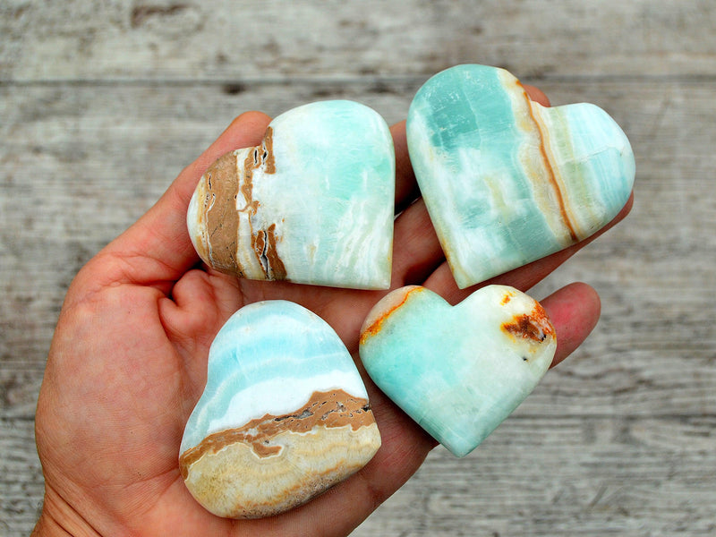 Four caribbean blue calcite crystal hearts 50mm-60mm on hand  with wood background