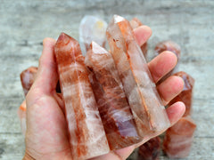 Three hematoid quartz points 100mm on hand with background with some stones on wood table