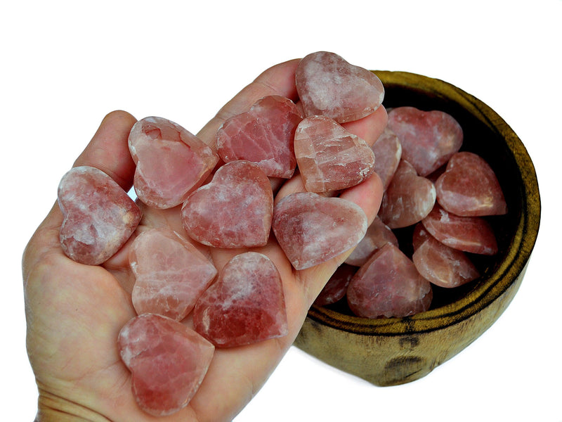 Ten rose calcite hearts 30mm-40mm on hand with background with some stones inside a wood bowl