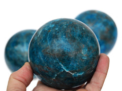 Extra large blue apatite sphere 85mm on hand with background with some stones on white