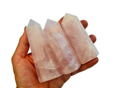 Three rose quartz crystal polished points on hand with white background