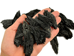 Some black kyanite stones 40mm-90mm on hand with background with some crystals n white