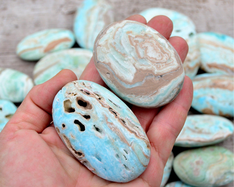 One blue aragonite palm stones 50mm-60mm mm on hand with background with some crystals