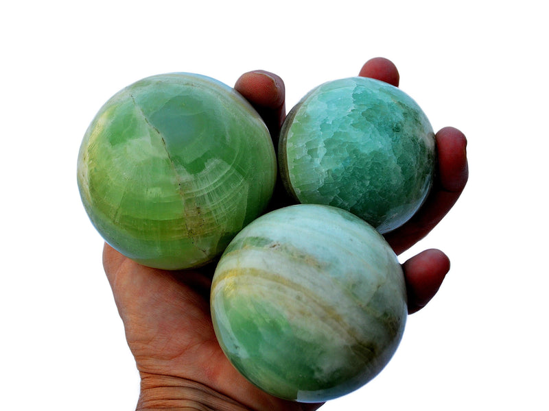 Three green pistachio calcite spheres 60mm-90mm on hand with white background
