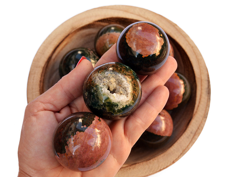 Three ocean jasper sphere crystals 45mm on hand with background with some crystal balls inside a wood bowl on white