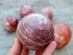 One rose calcite sphere crystal 70mm on hand with background with some balls on wood table