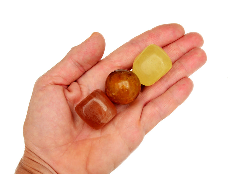 Small honey calcite and yellow calcite tumbled with golden healer quartz sphere on hand with white background
