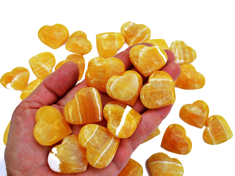 Ten orange calcite crystal hearts 30mm-35mm on hand with background with some hearts on white