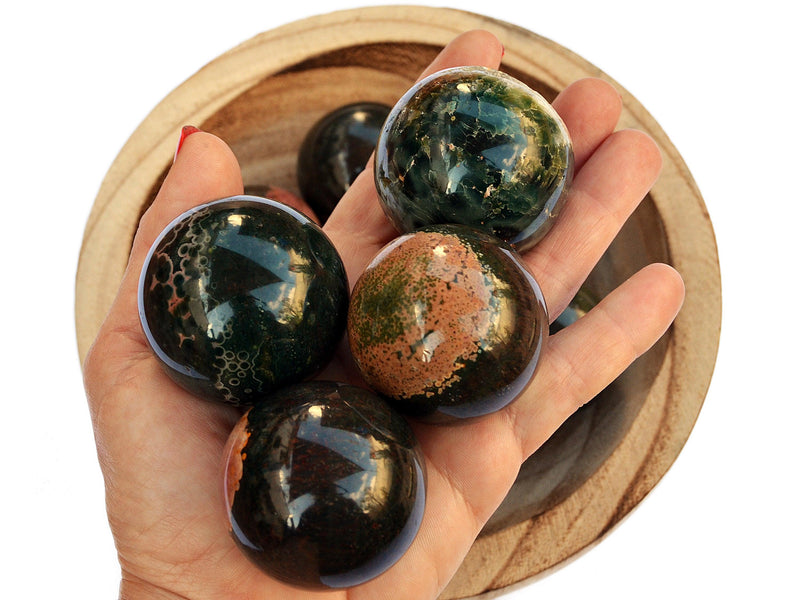 Four ocean jasper crystal spheres 45mm-55mm on hand with background with some crystals inside a wood bowl