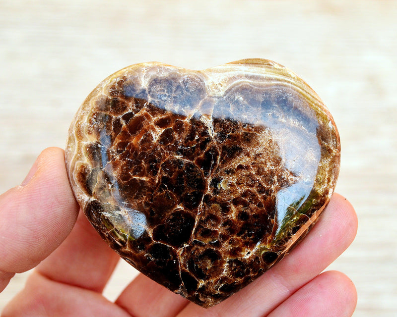 One chocolate calcite crystal carving heart 55mm on hand with wood background