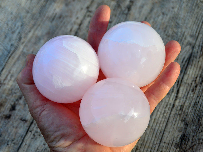 Three pink mangano calcite crystal spheres 60mm-65mm on hand with wood background