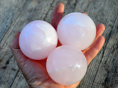 Three pink mangano calcite crystal spheres 60mm-65mm on hand with wood background