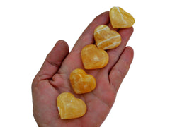 Five orange calcite crystal hearts 30mm-35mm on hand with white background 