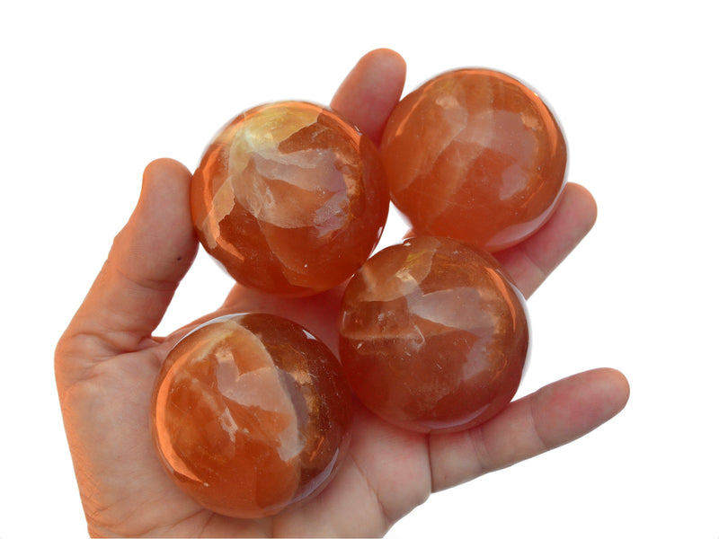 Four honey calcite crystal spheres 50mm on hand with white background