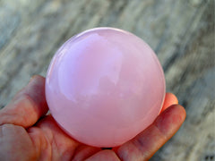 One large pink mangano calcite sphere 70mm on hand with wood background