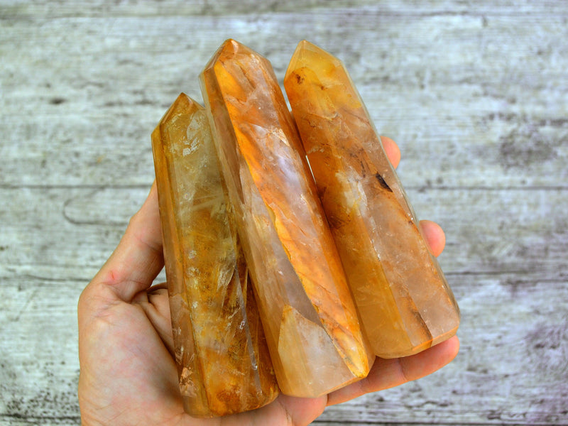 Three large golden healer crystal points 100mm-130mm on hand with wood background