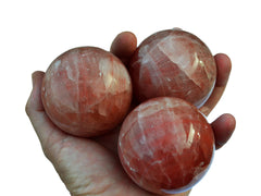 Three rose calcite sphere crystals 55mm-60mm on hand with white background
