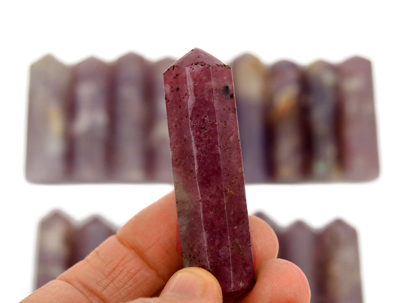 One lepidolite crystal point 50mm on hand with background with some stones on white