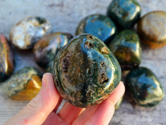 One green ocean jasper tumbled stone on hand with background with some minerals on wood table