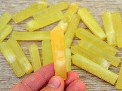 One yellow calcite crystal point 60mm on hand with background with several crystals on wood table