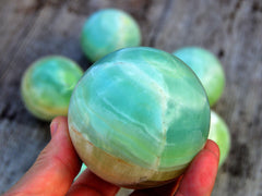 Large green pistachio calcite sphere 60mm on hand with background with some crystals on wood table