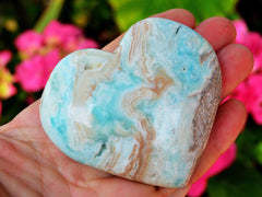 One large blue aragonite heartcrystal  85mm on hand with background with pink flowers