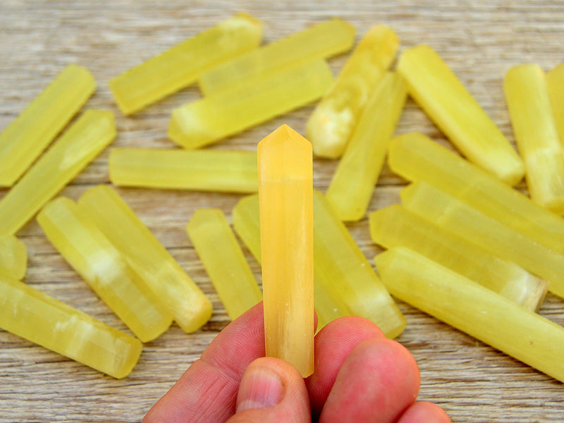 One yellow calcite crystal point 50mm on hand with background with several crystals on wood table