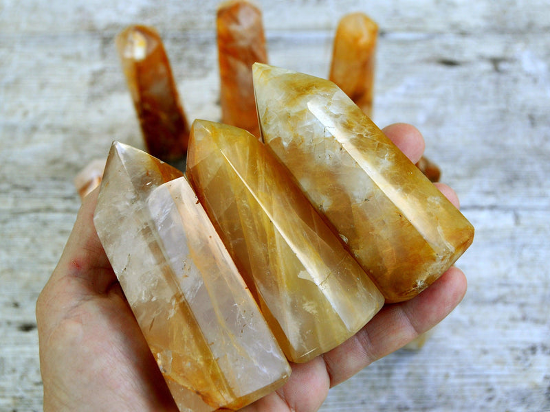 Three large yellow hematiud quartz towers on hand with background with some towers on wood