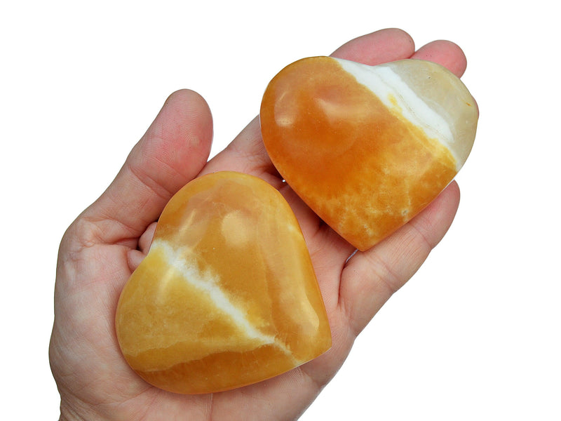 Two large orange calcite heart shapped crystals 60mm-65mm on hand with white background