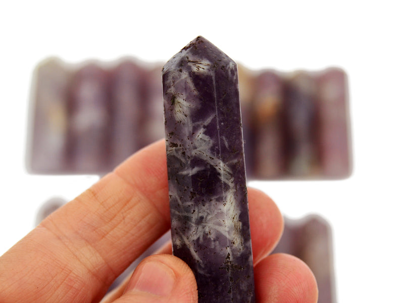 One lepidolite crystal point 60mm on hand with background with some crystals on white