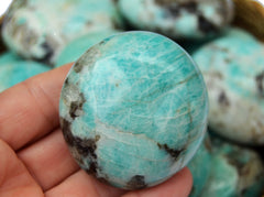 One green amazonite palm stone 60mm on hand with background with some crystals