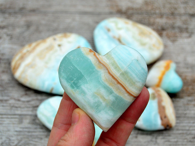 One caribbean blue calcite heart crystal 60mm on hand with background with some crystals on wood table