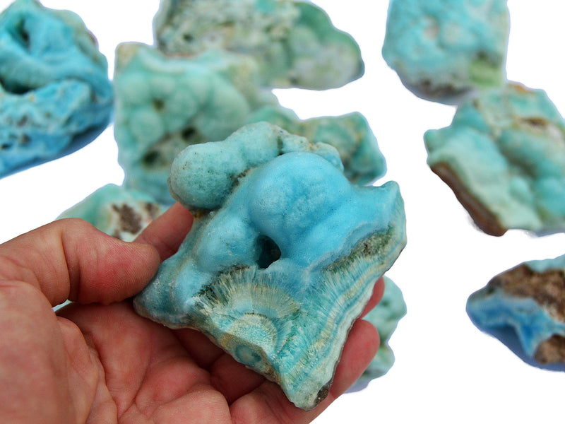 One rough blue aragonite crystal on hand with background with some stones on white