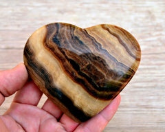 One chocolate calcite stone heart 75mm on hand with background with wood background