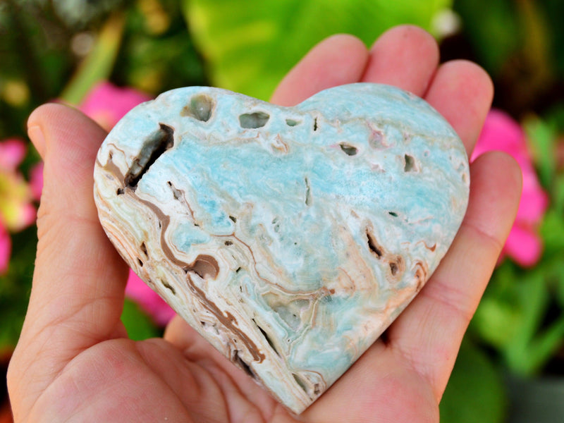 One large blue aragonite heart stone 70mm on hand with background with pink flowers