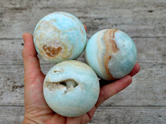 Three caribbean calcite crystal balls 60mm-65mm on hand with wood background