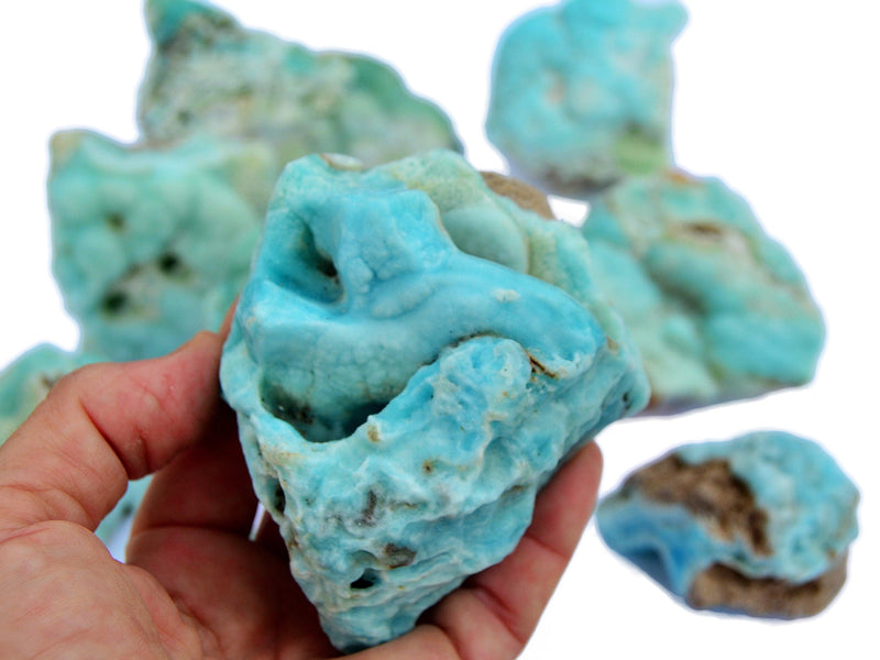 One blue aragonite raw on hand with background with some specimens on white