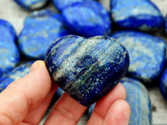 One lapis lazuli heart crystal 40mm on hand with background with some crystals on wood table