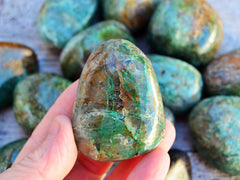 One big green chrysocolla tumbled crystal on hand with background with some minerals on wood table