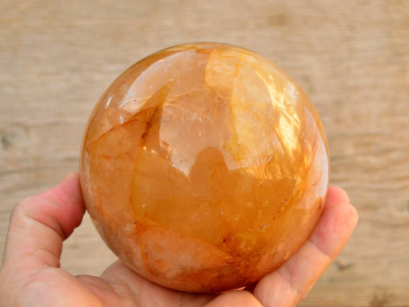 Large golden healer quartz sphere 90mm on hand with wood background