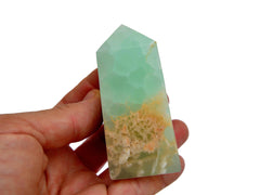 One green pistachio calcite tower 60mm on hand with white background 
