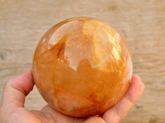 Large golden healer quartz sphere 90mm on hand with wood background