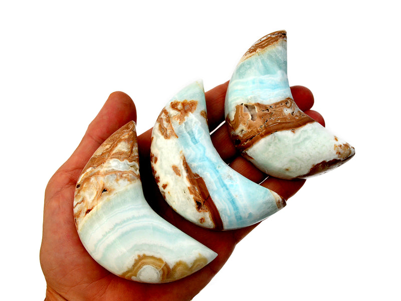 Three caribbean calcite shapped moon crystals 75mm on hand with white background