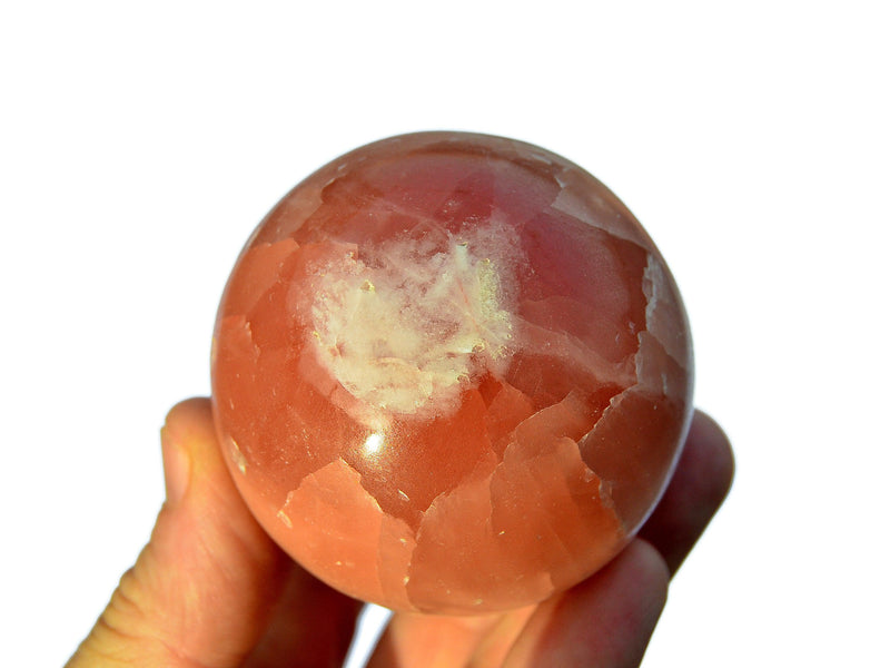 One rose calcite sphere stone 55mm on hand with white background