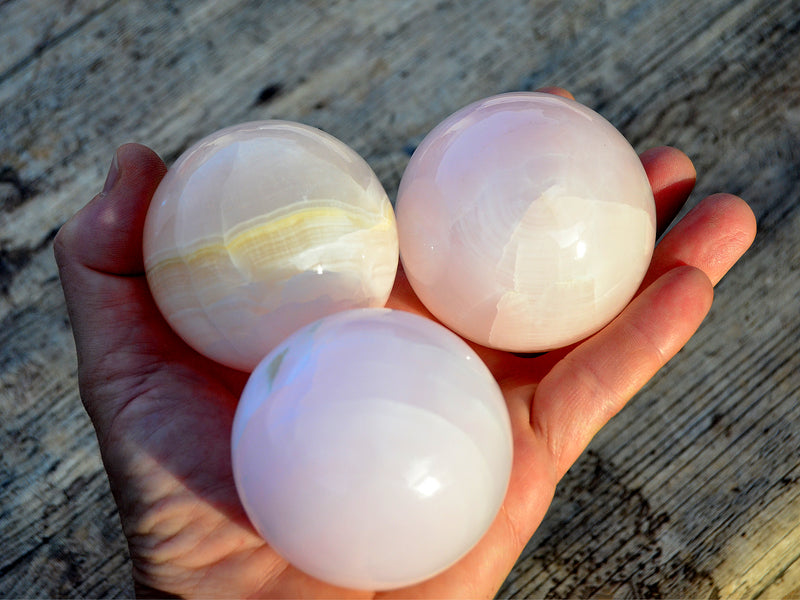 Three pink mangano calcite spheres 60mm-65mm on hand with wood background