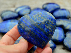 One lapis lazuli heart crystal 60mm on hand with background with some crystals on wood table