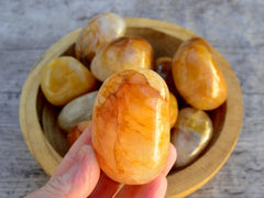 One large yellow hematoid crystal tumbled on hand with background with some stones on inside a wood bowl on wood table