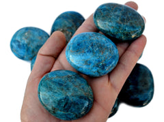 Three blue apatite palm stones 45mm on hand with background with some crystals on white