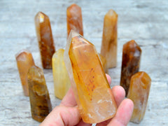 One chunky golden healer quartz generator on hand with background with several points on wood table